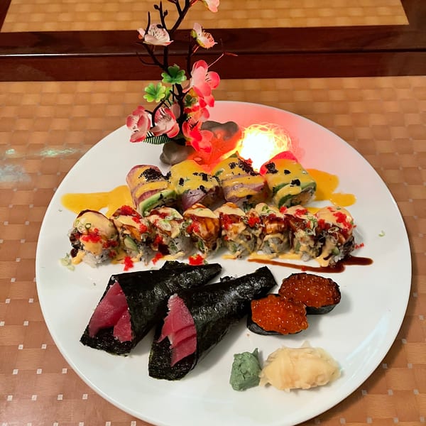 A white plate with various sushi rolls, tuna hand rolls, and salmon roe, garnished with a floral decoration.