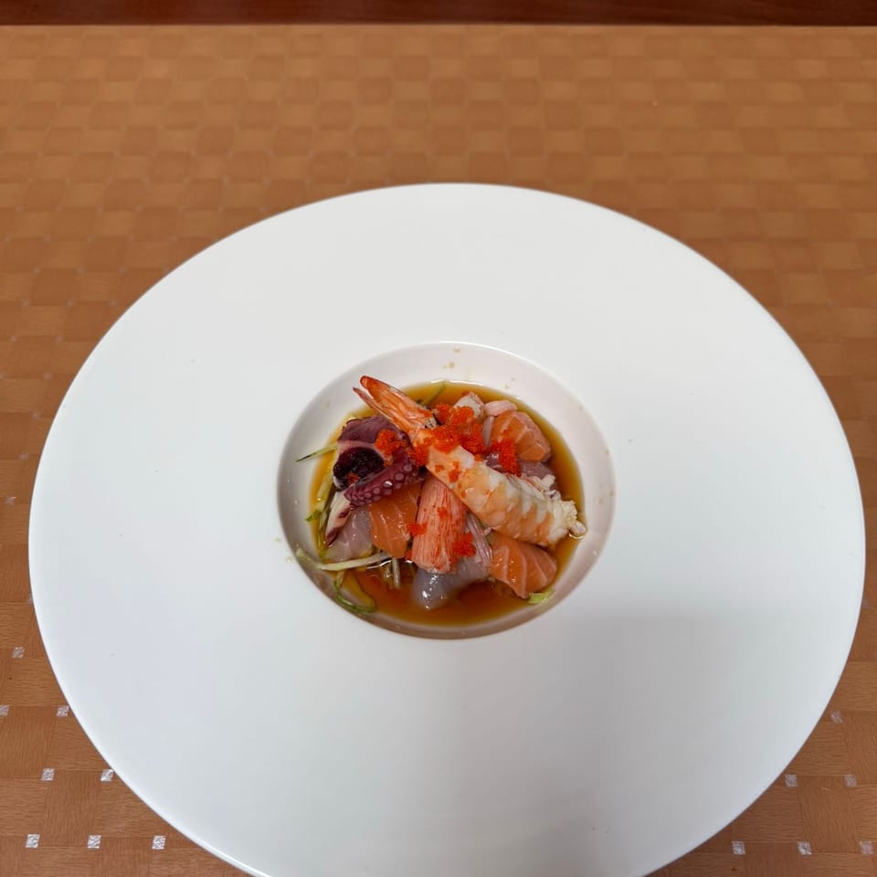 A white bowl filled with seafood, including shrimp, octopus, and salmon, garnished with roe.
