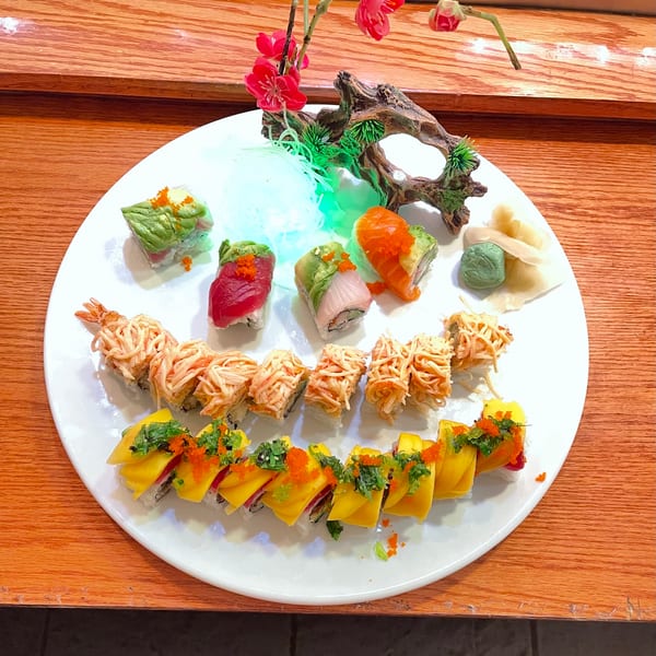 A white platter with various sushi rolls, including mango, crab, and tuna, on a wooden table.