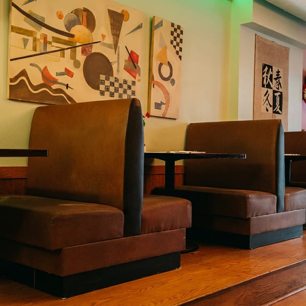 Restaurant interior with brown booths, small tables, abstract art, and a red balloon near a window.