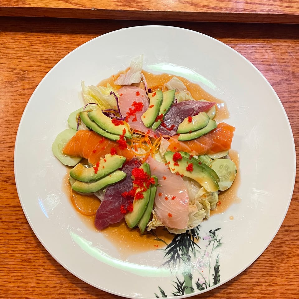 Colorful sashimi salad with salmon, tuna, avocado, cucumber, and red roe on a white plate.