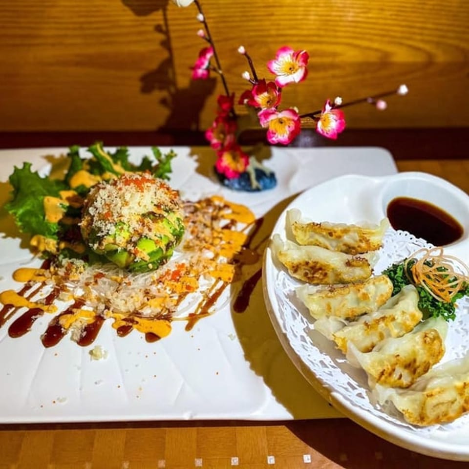 Avocado bomb sushi and pan-fried gyoza dumplings with dipping sauce and a floral decoration.