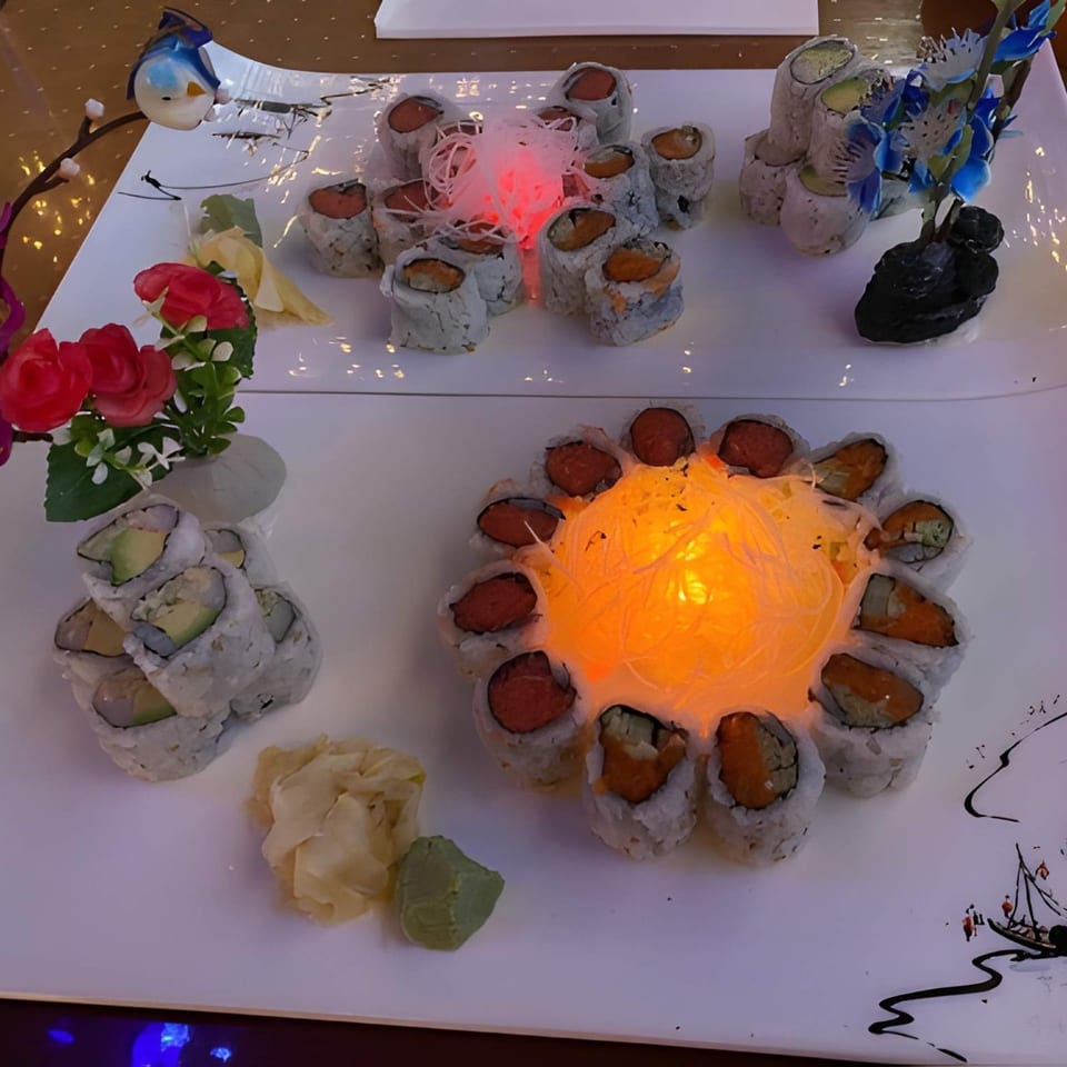 A large white platter with various sushi rolls, ginger, wasabi, and decorative elements.